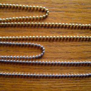 May include: Four ball chain necklaces in different lengths. The top two chains are gold, and the bottom two chains are silver.