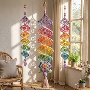 Puede incluir: Tres decoraciones colgantes en espiral hechas de hilo de ganchillo en un degradado de arcoíris de morado, rosa, naranja, amarillo, verde y azul. Cada pieza presenta recortes en forma de corazón, cuentas esféricas y un cordón central con borla.
