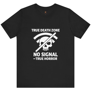 Può includere: T-shirt nera con grafica bianca raffigurante un teschio, un simbolo Wi-Fi sbarrato e il testo "TRUE DEATH ZONE" e "NO SIGNAL - TRUE HORROR". La maglietta ha girocollo e maniche corte.