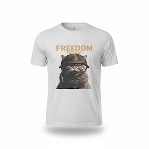 May include: Light gray t-shirt featuring a cat wearing a camouflage helmet. The text "FREEDOM FOR CAT" is printed above the cat's head in a tan color. The cat has a serious expression.