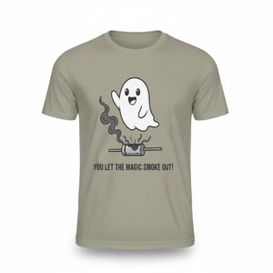 Könnte beinhalten: Hellgraues T-Shirt mit einem Cartoon-Geist, der über einem rauchenden Objekt winkt. Der Text "YOU LET THE MAGIC SMOKE OUT!" ist unter der Grafik aufgedruckt. Das Shirt ist aus weichem Material.