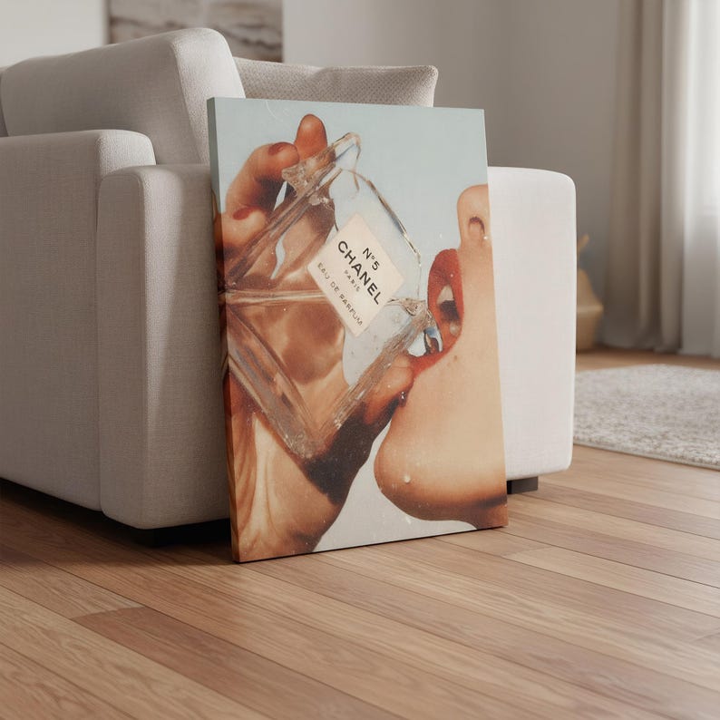May include: A canvas print featuring a close-up of a person's face with red lips, interacting with a Chanel No. 5 perfume bottle. The bottle is clear with white text. The background is a light blue.