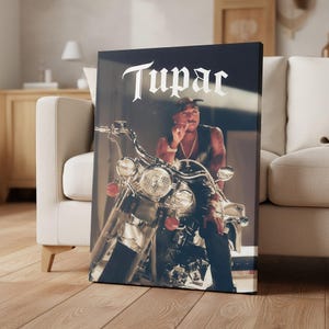 May include: Canvas print featuring a portrait of Tupac Shakur on a motorcycle. The image shows Tupac in a leather vest, with the word "Tupac" in white script at the top. The motorcycle has chrome details and red lights.