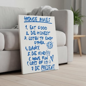 May include: A white canvas with blue handwritten text that reads "HOUSE RULES" followed by seven rules, including "EAT GOOD", "BE HONEST", and "DANCE". A disco ball graphic is included. The canvas is leaning against a gray sofa.