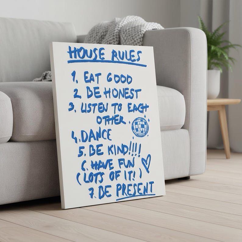 May include: A white canvas with blue handwritten text that reads "HOUSE RULES" followed by seven rules, including "EAT GOOD", "BE HONEST", and "DANCE". A disco ball graphic is included. The canvas is leaning against a gray sofa.