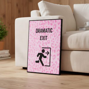 May include: A framed print featuring the words "DRAMATIC EXIT" in black. The background has a pink leopard print design. A black graphic of a person running towards an exit door is below the text.