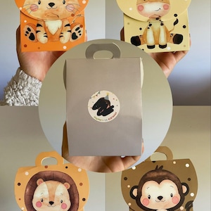 Puede incluir: Cuatro cajas de regalo con temática de animales con asas. Las cajas presentan un tigre, una jirafa, un león y un mono. También se muestra una caja de regalo plateada con una pegatina que dice "Jayden's 1st Birthday".