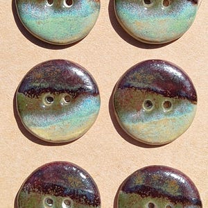 May include: A set of six round, two-hole buttons arranged in two columns on a tan card. Each button features a glossy, multi-coloured glaze with a dark brown top section, a muted green middle band, and a light, pale green base with subtle texture.