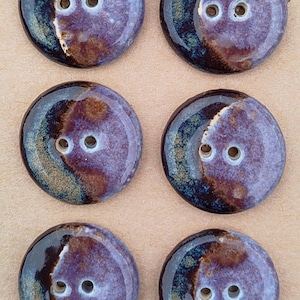 May include: A set of six round, two-hole ceramic buttons featuring a glossy glaze with blended shades of deep navy blue, purple, and earthy brown. The buttons are arranged in two columns on a tan card with the text Handmade ELIZA'S printed.