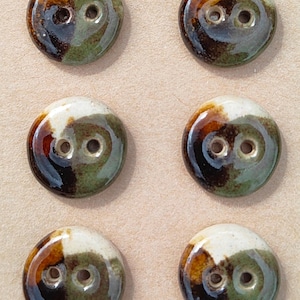 May include: Six round ceramic buttons arranged in two columns on a tan card. Each button features a glossy glaze with a marbled pattern of white, dark brown, and sage green. Each button has two central holes. The card is stamped with ELIZA'S BUTTONS.