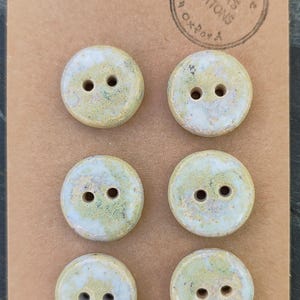 May include: Six handmade ceramic buttons with a speckled green and white glaze. Each button has two holes and is round. The buttons are on a brown card with the text "Handmade ELIZA'S BUTTONS in Oxford" printed on it.