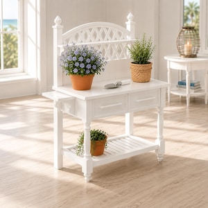 May include: A white potting bench with a lattice back panel, two drawers, and a lower slatted shelf. The bench holds a terracotta pot with purple flowers, a woven basket with a green plant, a small hand trowel, and a lower terracotta pot.