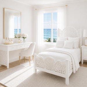 May include: A light and airy bedroom featuring white furniture and decor. The focal point is a white bed with an ornate headboard and footboard. A white vanity with a gold-framed mirror and a chair are on the left. The room has a view of the sea.