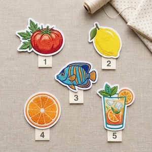May include: Embroidered patches featuring a tomato, lemon, fish, orange slice, and a cocktail. The patches are colorful with detailed stitching and white borders. Each patch has a small, numbered tag below it.