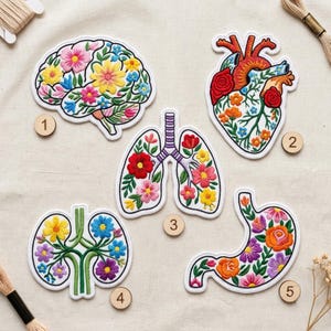 May include: Five embroidered patches featuring anatomical shapes filled with colorful floral patterns. The set includes a brain, heart, lungs, kidneys, and stomach, each labeled with a small wooden numbered disc from one to five.