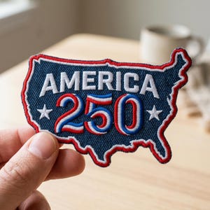 May include: Embroidered patch in the shape of the United States, with the word "AMERICA" in white block letters and the number "250" in red, white, and blue. The patch has a blue denim background and a red and white border. Two white stars are on the patch.
