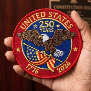 May include: A circular embroidered patch featuring a bald eagle holding an American flag. The text reads UNITED STATES, 250 YEARS, 1776, and 2026. The design uses red, white, blue, and gold thread on a circular fabric base with a red border.