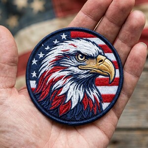 May include: Embroidered patch featuring a detailed bald eagle head with red, white, and blue colors. The patch is circular, with a blue border containing white stars and a background of red and white stripes.
