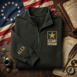 May include: A black quarter-zip sweatshirt with "ALEX" embroidered on the sleeve. The sweatshirt features a U.S. Army Veteran patch with a gold star and text. An American flag and historical documents are in the background.