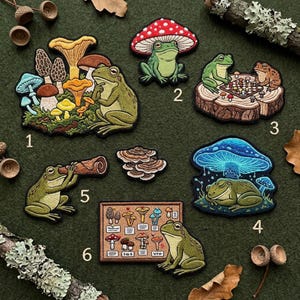 May include: A collection of six embroidered patches featuring frogs and mushrooms. The patches depict frogs with various mushroom designs, including a frog playing chess, and a frog looking through a telescope. The color palette includes green, red, and brown.