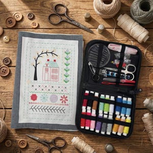Peut inclure: Une collection de fournitures de couture sur une surface en bois. Comprend une trousse de couture noire, de la broderie, des ciseaux, des bobines de fil, des boutons et un motif de point de croix d'une maison et d'un arbre. La palette de couleurs est neutre avec des touches de rouge, de vert et de bleu.