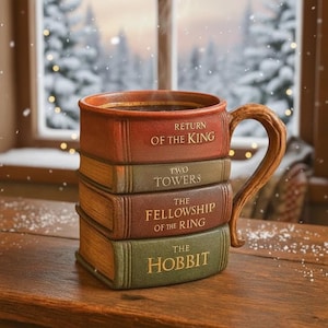 Puede incluir: Una taza de cerámica con forma de pila de libros, con los títulos "The Hobbit", "The Fellowship of the Ring", "Two Towers" y "Return of the King". La taza está llena de café y tiene un asa de madera. El fondo muestra una escena nevada.