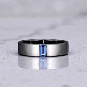 Könnte beinhalten: Ein silberfarbener Ring mit einem rechteckigen, hellblauen Edelstein in der Mitte. Der Ring hat ein flaches, poliertes Band und eine reflektierende Oberfläche, die einen modernen und eleganten Look erzeugt. Der Edelstein ist etwa 0,6 cm lang.
