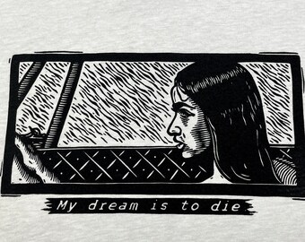 May include: Light gray t-shirt with a black and white graphic of a woman looking out a window. The text "My dream is to die" is below the graphic. The shirt has a crew neck and a tag that says "PCON CAVE 8".