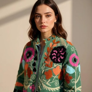 May include: A green jacket with colorful floral embroidery. The jacket features orange, pink, black, and blue flower designs, along with heart and leaf patterns. The jacket has a collared neckline and a striped shirt underneath.