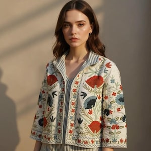 May include: Cream-colored jacket with floral embroidery in red, blue, and green. The jacket features a striped collar and cuffs, and a matching striped shirt underneath. The embroidery includes stylized flowers and leaf patterns, creating a detailed and colorful design.