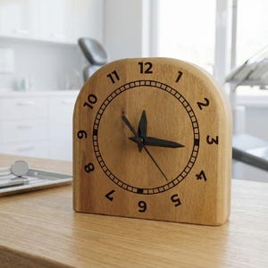 Puede incluir: Un reloj de escritorio de madera con un acabado marrón claro. La esfera del reloj tiene números y manecillas negras. El reloj está sobre un escritorio de madera con instrumentos dentales y un monitor de ordenador en el fondo.