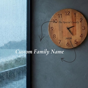 May include: A round wooden clock with black hands and large, clear numbers. The clock face includes the text "The Special Family" and the year "2026". The clock is mounted on a gray wall.