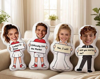 May include: Four custom-designed body pillows with cartoon faces and signs. The signs read: "Locked It Down," "Officially Off the Market," "Yes, I will!," and "Will you marry me?" The pillows are on a beige sofa.