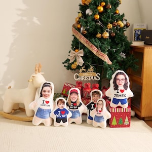 May include: Five custom-shaped plush pillows featuring printed faces and torsos with text including I LOVE CUSTOM, I LOVE MY GF, I LOVE MY BF, and I LOVE JAMES. The pillows are arranged in front of a decorated Christmas tree and a wooden rocking deer.