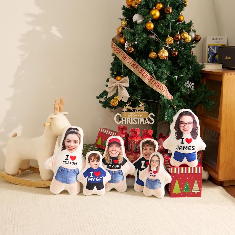 May include: Five custom-shaped plush pillows featuring printed faces and torsos with text including I LOVE CUSTOM, I LOVE MY GF, I LOVE MY BF, and I LOVE JAMES. The pillows are arranged in front of a decorated Christmas tree and a wooden rocking deer.