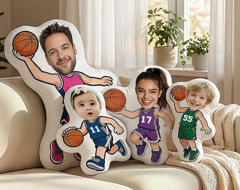 May include: Custom basketball-themed pillows featuring cartoon illustrations of people holding basketballs. Each pillow has a unique design with different jersey numbers and colors, including pink, purple, blue, and green. The pillows are on a beige sofa.