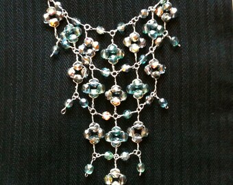 El collar babero iridiscente brillante presenta cuentas facetadas verdes y grises envueltas en plata esterlina.