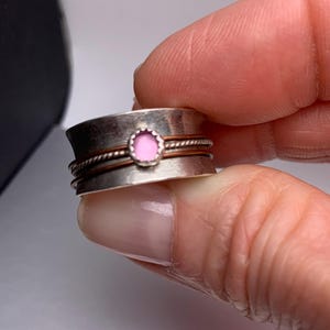 Könnte beinhalten: Ein silberner Ring mit einem rosafarbenen Glas Stein in der Mitte. Der Ring hat einen Kupferdraht umwickelt.
