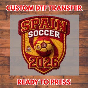 May include: A red and yellow Spain Soccer emblem with a soccer ball in the center. The emblem has the text "SPAIN SOCCER 2026" and the words "CUSTOM DTF TRANSFER" and "READY TO PRESS" in red.