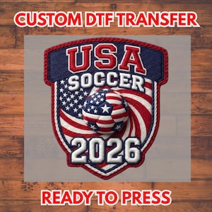 Può includere: Trasferimento DTF con un design a scudo con il testo "USA SOCCER 2026". Il design incorpora la bandiera americana e un pallone da calcio nei colori rosso, bianco e blu. È incluso anche il testo "CUSTOM DTF TRANSFER" e "READY TO PRESS".