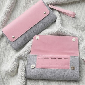 Puede incluir: Dos carteras de fieltro gris y rosa con un diseño de mando de videojuegos. Las carteras tienen una solapa y un interior rosas, con cierres de botón a presión plateados. Una cartera está abierta, revelando compartimentos interiores.