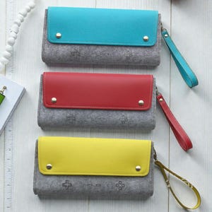 Può includere: Tre pochette in feltro in verde acqua, rosso e giallo con cinturini da polso abbinati. Ogni pochette ha un corpo grigio con un design a controller e una patta colorata fissata con borchie color oro. Le pochette sono rettangolari e sembrano essere in feltro.