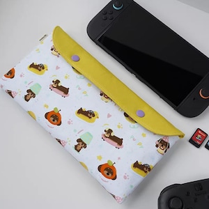 May include: A white and yellow patterned case for a gaming device. The case features a repeating pattern of cartoon dachshunds on skateboards, in hats, and in other playful poses. The case has a yellow flap with two purple snap closures.
