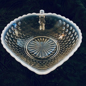 May include: A white milk glass bowl with a scalloped edge and a handle. The bowl has a textured surface with small raised dots and a central design of radiating lines.