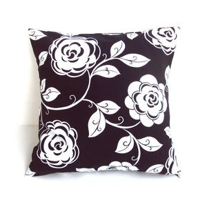 May include: Square decorative pillow with a black background and a white floral pattern. The design features large, stylized white roses and leaves with curved stems. The pillow is a square shape, perfect for a couch or bed.