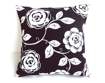 May include: Square decorative pillow with a black background and a white floral pattern. The design features large, stylized white roses and leaves with curved stems. The pillow is a square shape, perfect for a couch or bed.