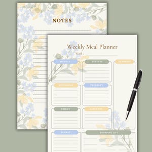 Puede incluir: Un planificador de comidas semanal y una página de notas con detalles florales. El planificador de comidas tiene secciones para cada día de la semana, una lista de compras y una sección de recordatorios. Un bolígrafo negro descansa sobre el planificador.