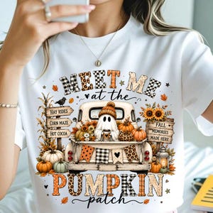 Puede incluir: Una camiseta blanca con un gráfico de un camión antiguo que transporta un fantasma con gorro, rodeado de calabazas, girasoles y letreros que dicen "MEET ME at the PUMPKIN patch", "HAY RIDES", "CORN MAZE", "HOT COCOA" y "FALL MEMORIES MADE HERE".