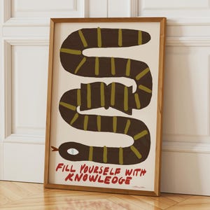Può includere: Una stampa artistica da parete rettangolare incorniciata che raffigura un serpente marrone scuro con strisce verde oliva avvolto attorno a un libro aperto. Il testo "FILL YOURSELF WITH KNOWLEDGE" è stampato in rosso sul fondo bianco sporco.