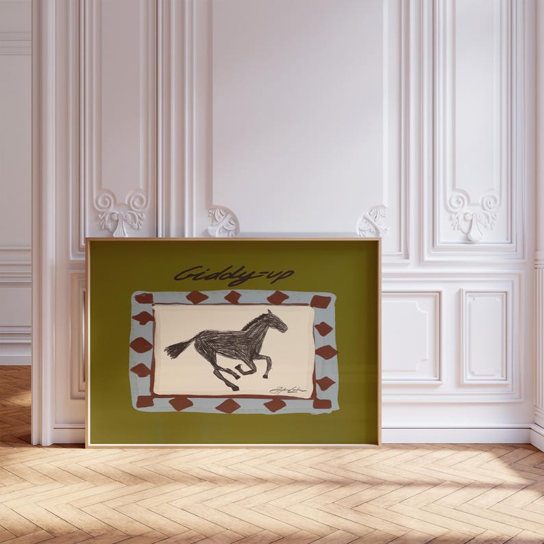 western chartreuse poster in frame showing a sketch of a horse galloping in a blue and red diamond border, in script it says "giddyup"